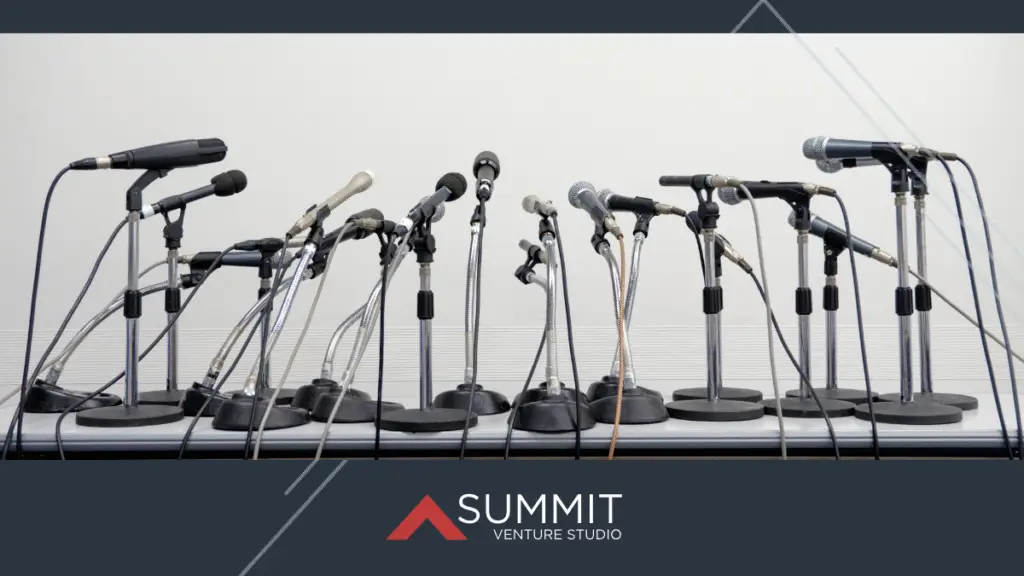 A lineup of assorted microphones on stands arranged in a semicircle on a table, suggesting a press conference setup. The Summit Venture Studio logo is displayed at the bottom of the image.